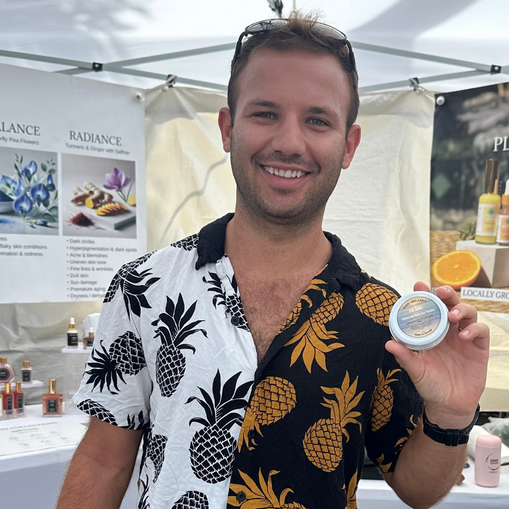 Man in pineapple-patterned shirt holding a product container at an outdoor event.