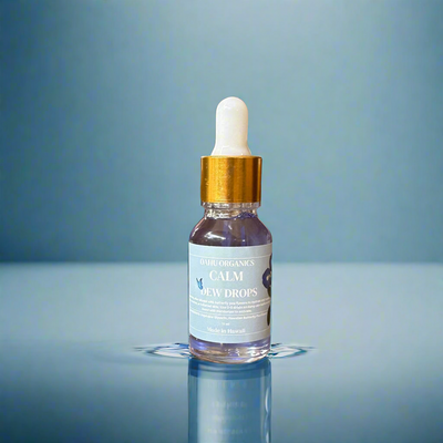 Bottle of 'Calm' dew drops with a gold cap on a reflective surface and blue background